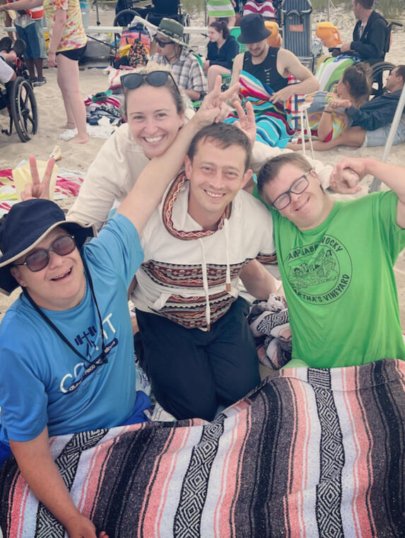 Four people sit on the beach smiling at the camera